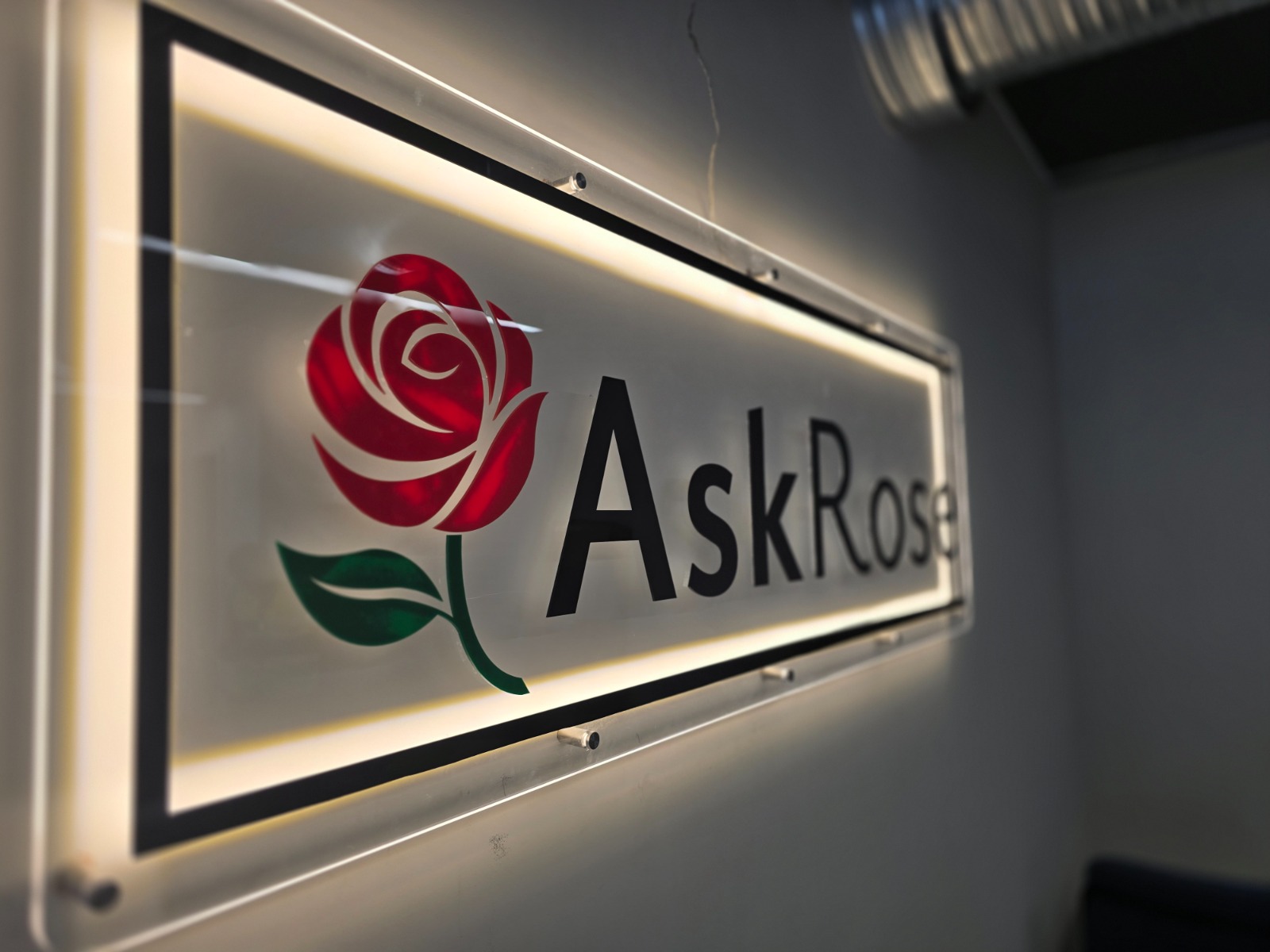 Angled close-up of the illuminated Ask Rose logo sign
