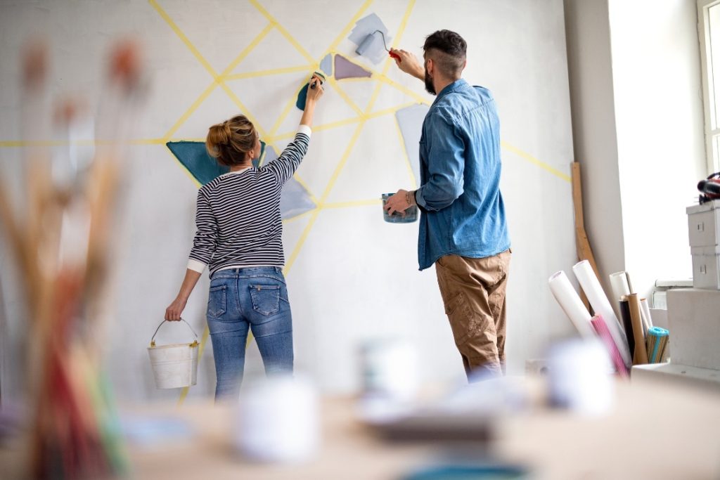 A man and woman collaboratively painting a colorful mural on a wall, showcasing their creativity and teamwork
