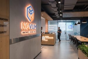 (Contemporary office lobby with an illuminated, dimensional NOVUM logo wall and reception desk displaying the tagline "INNOVATE. DESIGN. BUILD.", illustrating the integration of signage and brand messaging.)